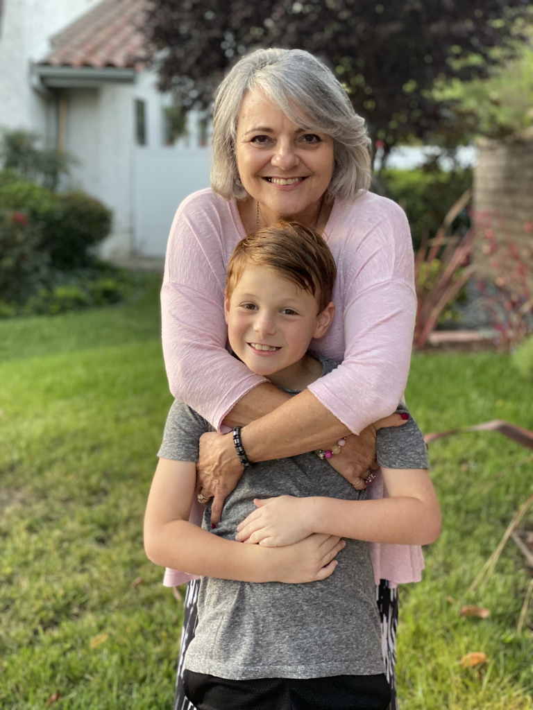 Regine Swim, native French tutor in San Diego, smiling in a garden with her grandson